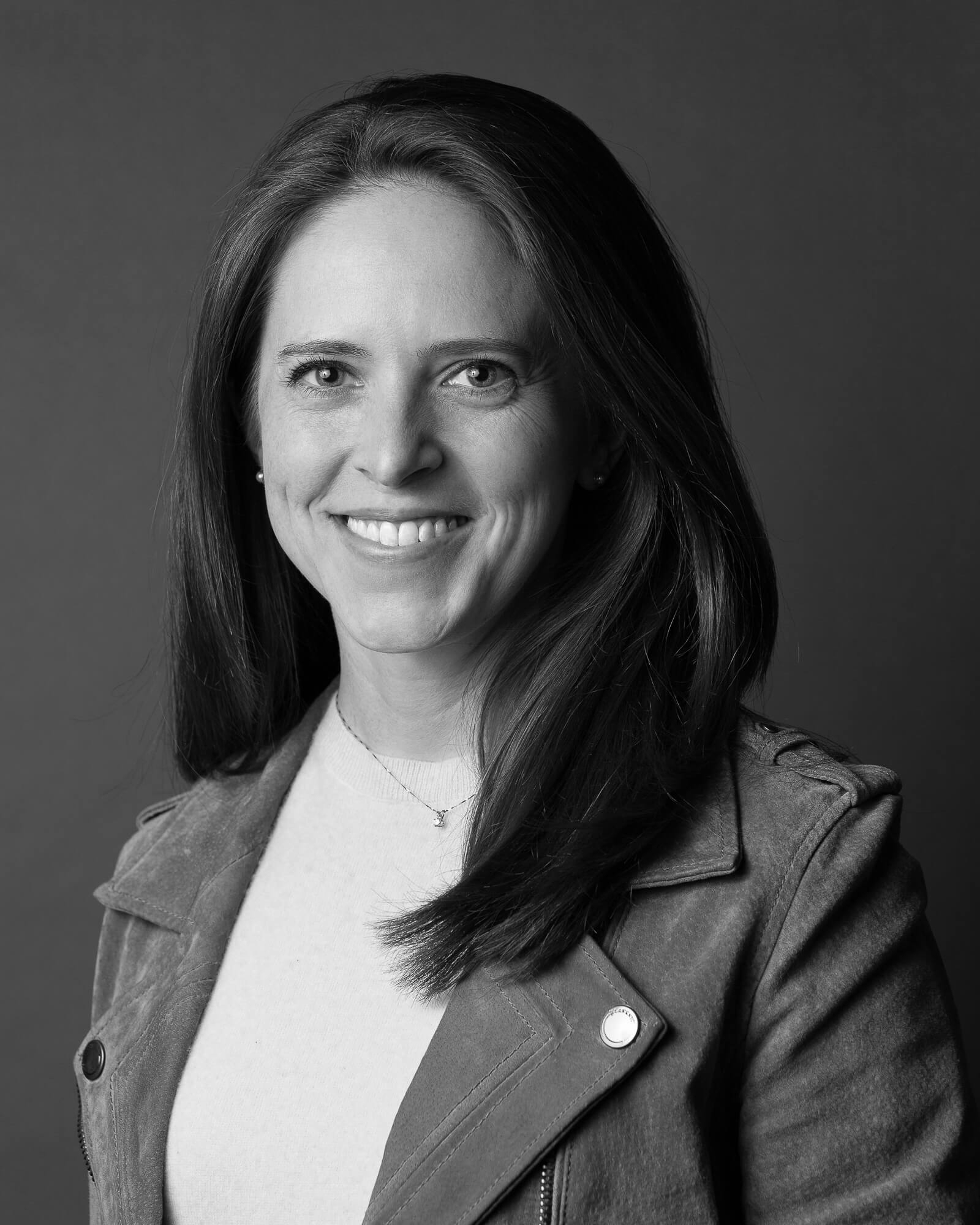 Black and white portrait of a smiling woman with long hair, wearing a jacket over a light top.